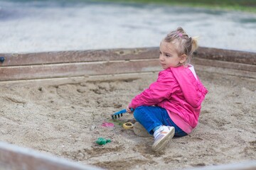 Little cute blond girl playing alone in the childrens playground in the park.