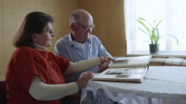 senior couples keeping love and care for each other are inspired by memories of past years, looking at photos in family photo album sitting at table