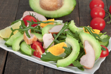 Avocado salad with rucola, mixed vegetables and chicken  on rustic wooden table. Healthy food concept.