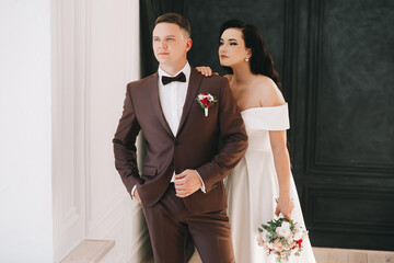 Bride and groom. Close up portrait of a man in a suit and a brunette woman in a white wedding dress. Indoors or in the studio, on the wedding day. European appearance. Hug, hold hands.