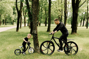 Obraz premium Happy little boy rides a bike with a young dad in the Park