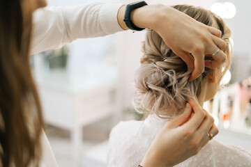 Fototapeta premium Close-up of hairdresser making hairstyle unrecognizable young blonde woman in beauty salon, back view. Concept of beauty, fashion and stylish makeup.