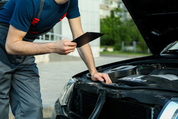 A man in overalls holds clipboard. Mechanic. Car inspection