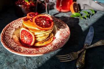 Fototapeta na wymiar Vintage plate with pancakes with blood orange slices, red sauce and pomegranate seeds on dark background.
