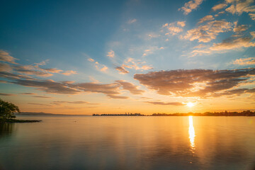 Sonnenuntergang über der Insel Lindau im Bodensee mit orangeroter Sonne und blauem Himmel, glatte...
