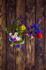 Fototapeta na wymiar field flowers of many colors on wooden background