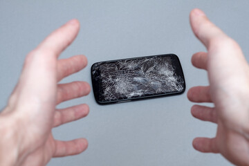 Man dropping his smartphone and trying to reach it. Phone screen is cracked and needs repairing