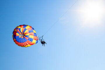 Two people on a parachute flies over the sea in the blue sky. Beach entertainment