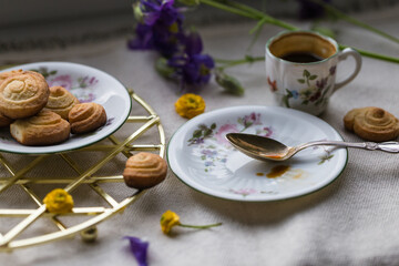 Delicate porcelain coffee set with espresso and homemade cookies, spoon and spring flowers on linen fabric.