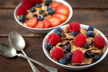 Granola with blueberries and raspberries in white bowl in dark wooden desk.