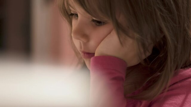 Charming little girl drawing with pencil on her school desk and watching tablet, selective focus