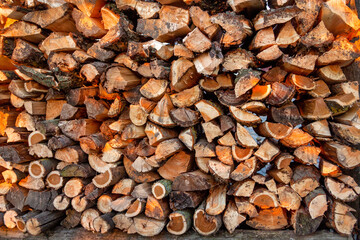 Firewood background. Preparation of firewood for the winter and use for cooking. Stacks of firewood with sun spots.