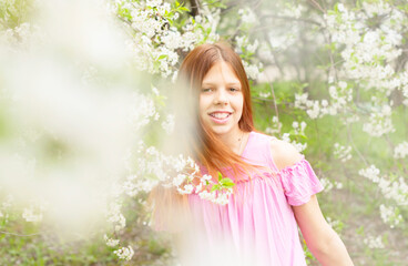 red-haired teen girl having fun in a blooming cherry orchard, the concept of spring and the end of the quarantine