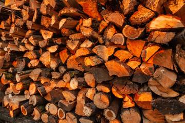 Firewood background. Preparation of firewood for the winter and use for cooking. Stacks of firewood with sun spots.