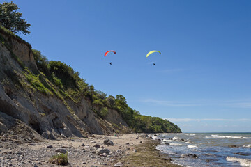 Two paragliders are flying over the wild steep coast on the beach of the Baltic Sea on a sunny day, beautiful landscape for outdoor sports and vacations, blue sky with copy space