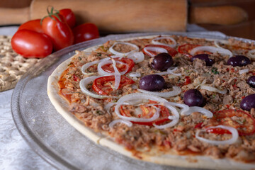 .Pizza of Brazilian cuisine with tuna stuffing with onion and olives, blurred background of tomatoes and wooden cylinder and bricks