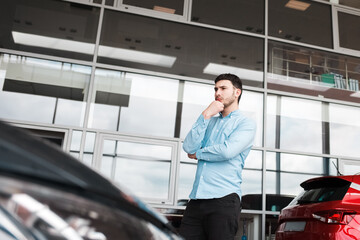 Fototapeta premium Pensive man looks at cars at a auto dealership