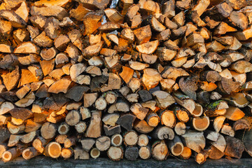 Firewood background. Preparation of firewood for the winter and use for cooking. Stacks of firewood with sun spots.