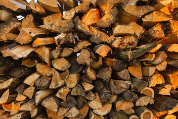 Firewood background. Preparation of firewood for the winter and use for cooking. Stacks of firewood with sun spots.