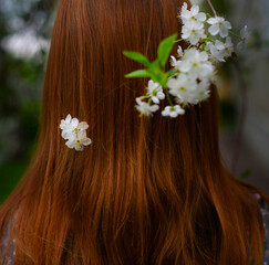 Naklejka premium a red-haired girl stands from back in a blooming garden with flowers in her hair