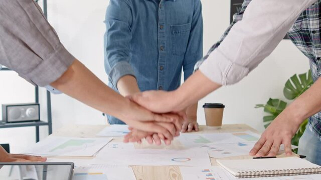 Group of young adult Asian business people join hands stacking and clap together in team meeting. Startup small business office, success teamwork celebration, happy work life concept