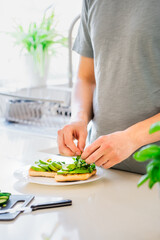 Close up man hands making a healthy meal of avocado toast and vegetables putting just picked greenery from homegrown garden on kitchen. Breakfast idea. Vegetarian and vegan diet. Vertical. Copy space.