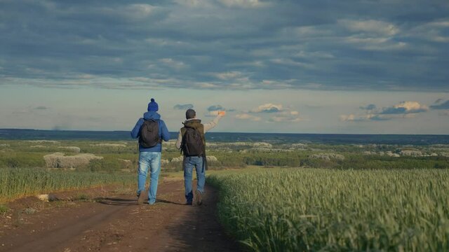 teamwork travel. two man hikers with backpacks walk along a trail next to a field with green grass in nature. concept adventure travel hiking healthy lifestyle. two tourists lifestyle walk walking
