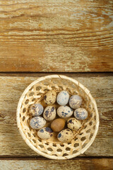 Fresh quail eggs in a wicker basket on a wooden rustic table.