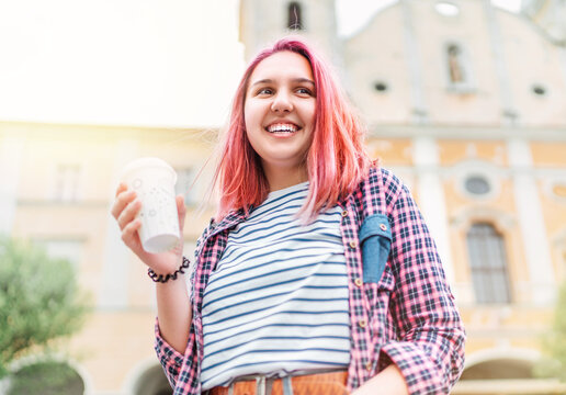 Portrait of cheerfully smiling Beautiful modern young female teenager with extraordinary hairstyle color in checkered shirt holding "coffee to go" cap.  Modern teens or cheerful students concept image