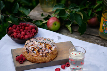 Apple pie on an old wooden table under an apple tree in a village. Bright sunny day and tasty homemade dessert with compote.