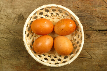 Chicken eggs in a wicker plate on a wooden table.
