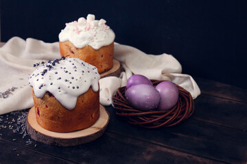 Easter cakes on a dark background, decorated with lavender and marshmallows, and painted Easter eggs in a wicker nest