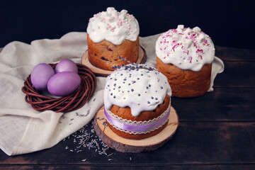 Easter cakes on a dark background, decorated with lavender and marshmallows, and painted Easter eggs in a wicker nest.