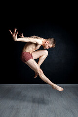 Contemporary dance positions. Young man is jumping with his hands behind his back and leg in passe compose.