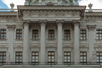 Fragment of the facade of a gray old building with carved columns and many windows