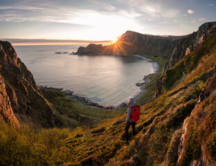 A woman hiking during midnight sun. Active vacation in Norway. Located on Andøya island in Vesterålen north of Norway. Sunset and backpack girl. - obrazy, fototapety, plakaty