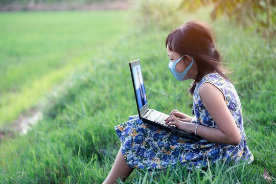 Happy Little Child Girl Learning Outdoor By Studying Online And Working On Laptop In Green Field With Wearing Face Mask