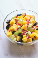 Fruit salad in a transparent glass bowl on a white wooden table.