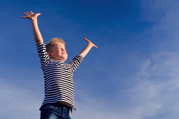 Relaxed boy breathing fresh air raising arms over blue sky at summer. Dreaming, freedom and...