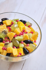 Fruit salad in a transparent glass bowl on a white wooden table.
