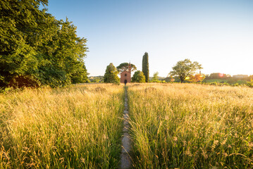 Plakat Red church Pomelasca in Brianza Inverigo in Lombardy Italy at sunset with the sum warm light and grass meadow and cypresses