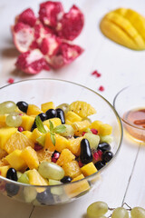 Fruit salad in a transparent glass bowl on a white wooden table.