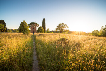 Red church Pomelasca in Brianza Inverigo in Lombardy Italy at sunset with the sum warm light and grass meadow and cypresses
