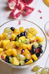 Fruit salad in a transparent glass bowl on a white wooden table.