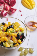 Fruit salad in a transparent glass bowl on a white wooden table.