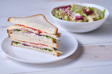Sandwiches with lettuce, ham, cheese and tomato on a white wooden table.