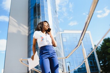 Content formal African American woman in suit standing on sidewalk on street and reading papers in file against contemporary building