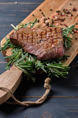 Freshly cooked steak on rosemary branches. The dish is served on a large wooden board. Close-up.
