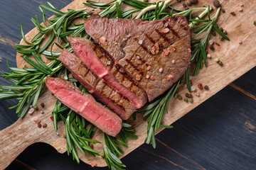 Sliced freshly cooked steak with blood, served on the branches of fresh rosemary on a wooden board. Close-up. Top view.
