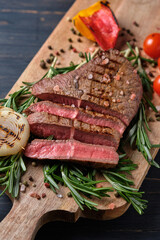 Sliced freshly cooked steak with blood, served with grilled vegetables and fresh rosemary on a wooden board. Close-up.
